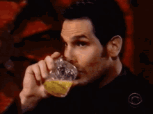 a man is drinking a glass of orange juice with a cbs logo on his shirt