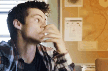 a young man in a plaid shirt is drinking from a glass .