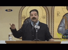a man stands at a podium giving a speech in front of a wall with icons and the letter mp on it