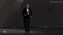 a man in a tuxedo is standing in front of a microphone at an emmys