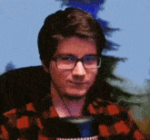 a man wearing glasses and a plaid shirt is smiling while sitting in front of a microphone .