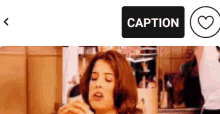 a woman is eating a sandwich in a kitchen with a caption button below her