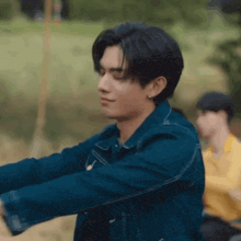 a man in a blue jacket is stretching his arms in a park .