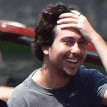 a man in a gray shirt is smiling and holding his hand to his head