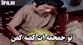 a man is sitting on a couch with his head in his hands and a foreign language written on the bottom of the image .