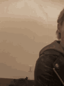 a man in a leather jacket is standing in front of a white wall
