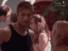 a man in a black tank top stands next to a woman in a white shirt in a scene from zone romantico