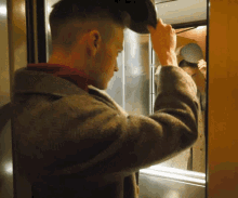 a man in a brown coat is adjusting his hat in front of a mirror