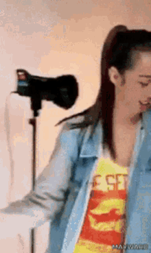 a woman in a denim jacket is standing in front of a camera while wearing a shirt that says e set