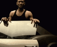 a man in a black tank top is standing next to a car