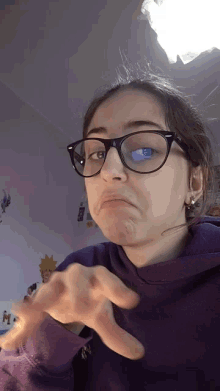 a girl wearing glasses and a purple hoodie is making a face