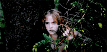 a girl with long hair is peeking out from behind a tree