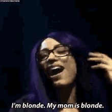 a woman with purple hair and glasses is saying `` i 'm blonde , my mom is blonde . ''