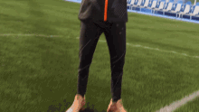 a person standing on a soccer field wearing black pants and orange stripes