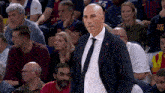 a bald man in a suit and tie stands in front of a crowd wearing a number 23 shirt