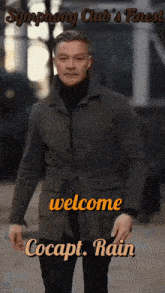 a man in a coat is standing in front of a sign that says welcome cocapt. rain