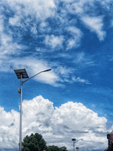 a street light with a solar panel attached to it against a cloudy blue sky