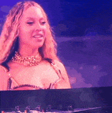 a woman wearing a gold necklace is smiling in front of a piano