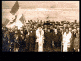 a black and white photo of a group of men standing in front of a flag