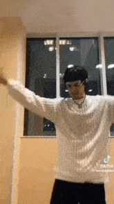 a man in a white sweater and headphones is dancing in a room .