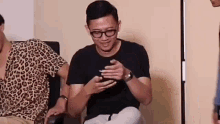 a man in glasses is sitting in a chair looking at his cell phone .