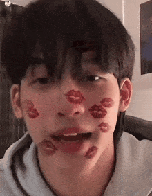 a young man with red kisses on his face is making a funny face .