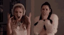 two women are screaming and covering their mouths while standing next to each other in a dark room .