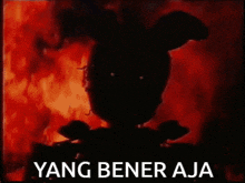 a silhouette of a rabbit is standing in front of a fire with the words `` yang bener aja '' written below it .