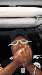 a man wearing glasses and a nfl jersey holds something in his mouth