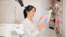 a woman is standing in front of a sewing machine and holding a piece of fabric