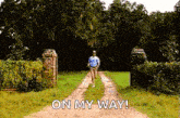 a man is walking down a dirt road with the words on my way written on the side .