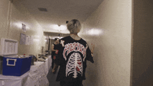 a man wearing a black shirt with a skeleton design on the back is walking down a hallway