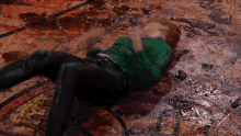 a man in a green shirt is laying on a dirty floor