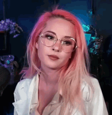 a woman with pink hair and glasses is wearing a white coat and a white shirt .