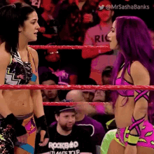 two female wrestlers are standing in a wrestling ring and talking to each other .