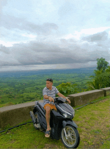 a man is sitting on a motorcycle with a view of a lush green valley in the background