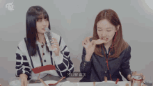 two girls are sitting at a table with a twice logo on the bottom left