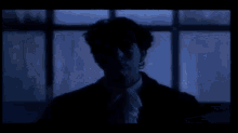 a man in a suit is standing in front of a window in the dark .