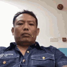 a man with a piercing in his lip is wearing a denim shirt and sitting on a couch .