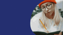 a woman wearing glasses and a beanie is writing in a notebook