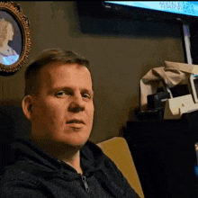 a man sitting in front of a tv with a picture of a woman in a frame behind him
