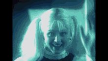 a woman with pigtails is smiling and waving at the camera in a dark room .