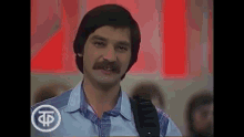 a man with a mustache is standing in front of a red sign .