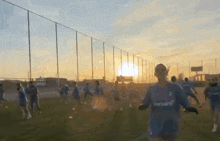 a man in a blue herbalife shirt is running on a field at sunset