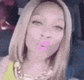a woman with blonde hair and pink lips is blowing a kiss while wearing a necklace .