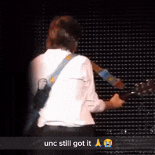 a man playing a guitar on a stage with the words " unc still got it " below him