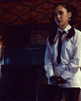 a woman in a white shirt stands in a dark room with a patterned ceiling