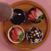 four cupcakes with strawberries and chocolate on a wooden plate with easy plus written on the bottom