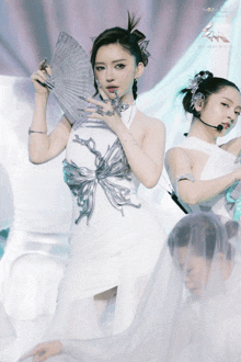 a woman in a white dress holds a fan while another woman stands behind her