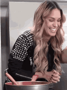 a woman in a studded jacket is holding a bowl and smiling .
